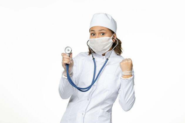 套装正面图女医生穿着白色的医疗服 戴着口罩 在白墙上用听诊器给潘多米病毒治病药品听诊器使用
