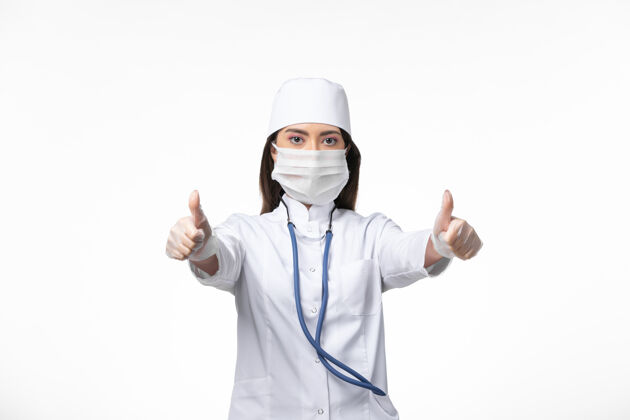 男性正面图：女医生穿着白色无菌医疗服 带着口罩 因为柯维德在白墙上摆姿势 传染柯维德大流行病毒病冠状病毒面具医生