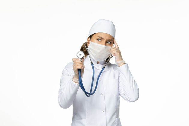 药正面图女医生穿着白色医疗服 戴着口罩用听诊器思考白墙大流行病毒病的医学女性人医生