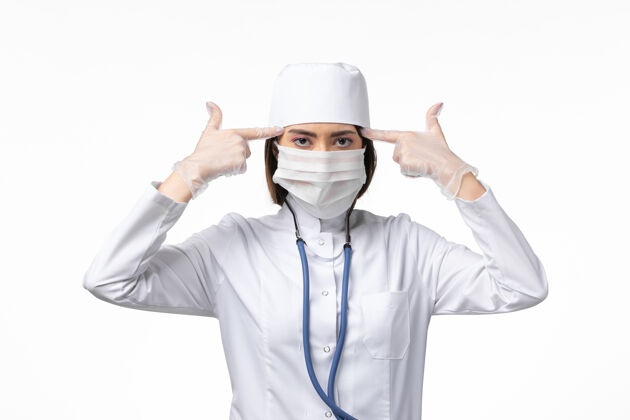病毒正面图女医生穿着白色医疗服 戴着口罩 由于白墙上大流行疾病 医学病毒大流行医学套装医生