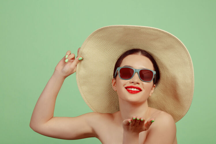 帽子美丽女人的肖像 明亮的妆容 红色的眼镜和帽子在绿色空间时尚和时尚的制作 发型美丽 时尚和广告概念明亮化妆向上
