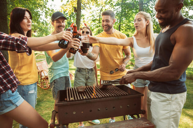 野餐一群快乐的朋友在阳光明媚的日子里喝着啤酒 一起烧烤一起在户外的林间空地或后院休息自然男人酒精