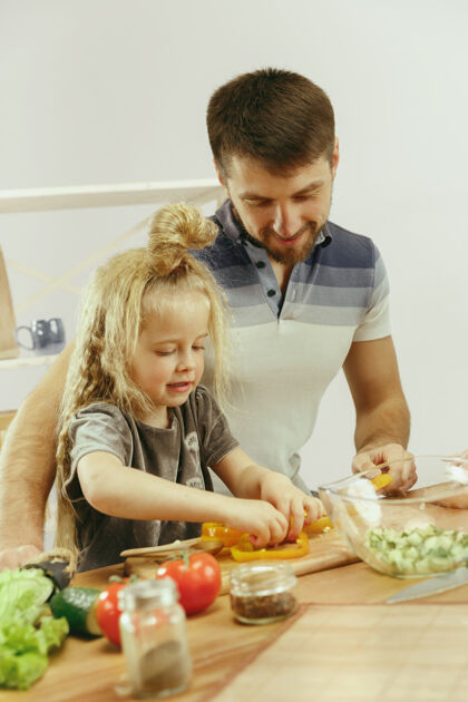 沙拉可爱的小女孩和她美丽的父母在家的厨房里切蔬菜 一边微笑着做沙拉吃饭食物吃