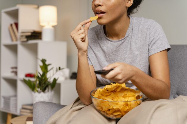 薯片坐在沙发上看电视吃薯片的女人女人零食休闲