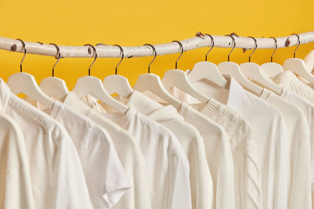木头白色女装挂在衣架上的水平镜头 隔离在黄色背景上穿着女装的更衣室衬衫白色高领毛衣
