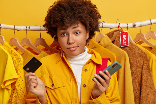购物者消费主义 购物和生活方式的概念无知的卷发女人拿着信用卡和手机包卡付款