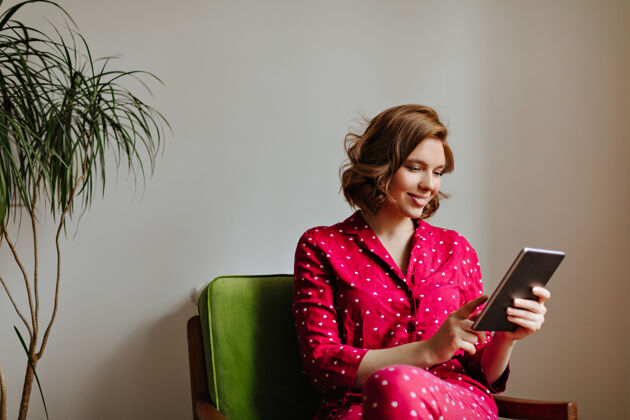 女性穿着睡衣的快乐女人微笑着使用数码平板电脑穿着红色睡衣的女人拿着小玩意的室内镜头年轻人房间情感