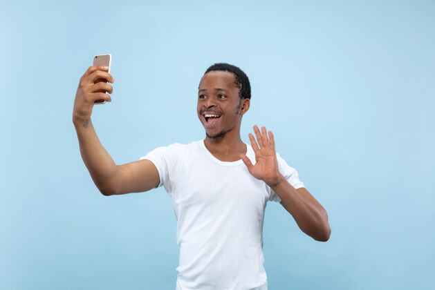 人类半身特写肖像的年轻非洲裔美国男子在白色衬衫的蓝色空间人类的情感 面部表情 广告概念就业企业家男性