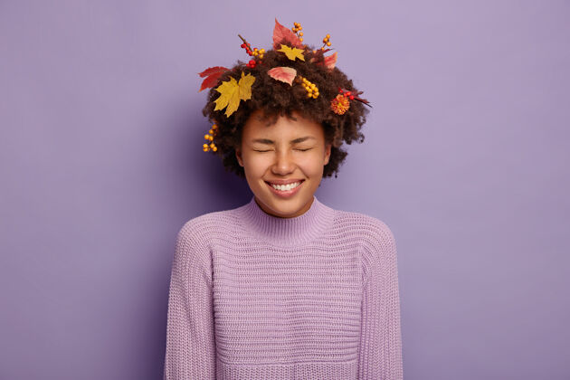 美国喜出望外的卷发女人开怀大笑 有秋天的心情 笑容灿烂 和朋友开玩笑 头发上有黄色的枫叶和浆果 穿着休闲服幸福 幸福紫色叶子卷发