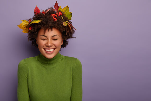 女人喜出望外的非洲裔美国女人有着独特的外表 微笑温柔 穿着新衣服 卷发 在紫色背景下的摄影棚里摆姿势 手放在身上非洲浆果欢呼