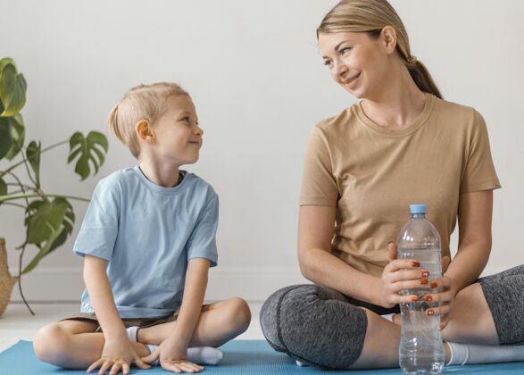 健康坐在垫子上的一个女人和一个小孩全速私人教练锻炼