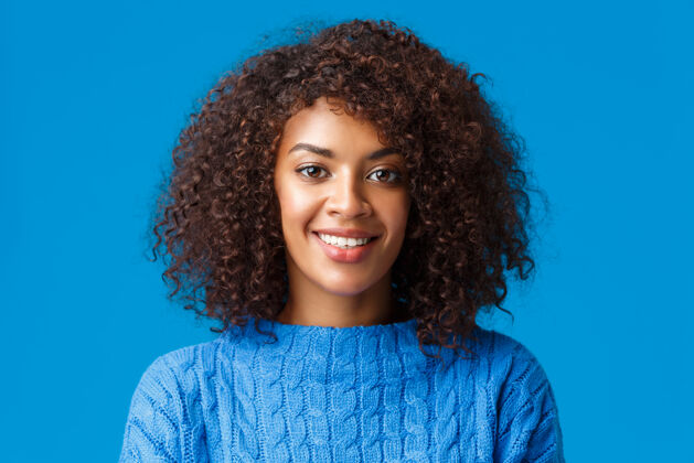 举行特写写真可爱的非洲裔美国年轻女子 卷发 非洲式发型 微笑着愉快的表情 享受着寒假 穿着毛衣 蓝色的墙壁女朋友非洲女性