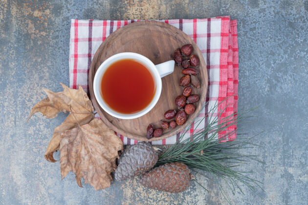 茶一杯红茶和干玫瑰果放在松果木盘上高质量的照片饮料桌布松果