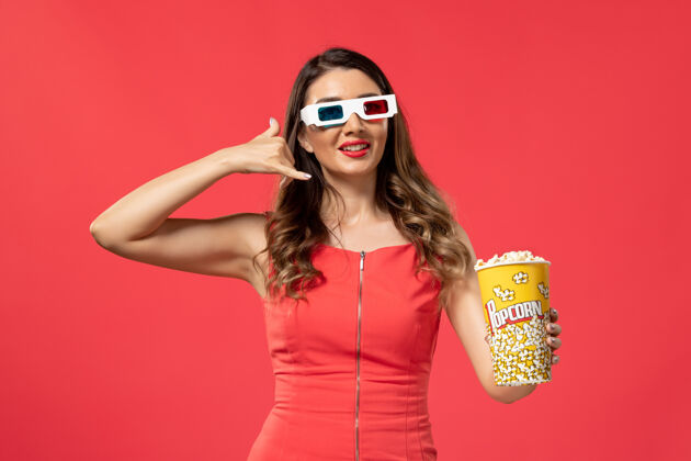 抱正面图年轻女性手持爆米花包戴着d墨镜在红色表面太阳镜电影院前面