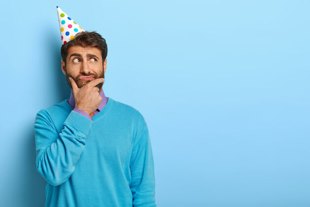 困惑一个戴着生日帽 穿着蓝色毛衣的沉思男人的摄影棚照片男人领带节日