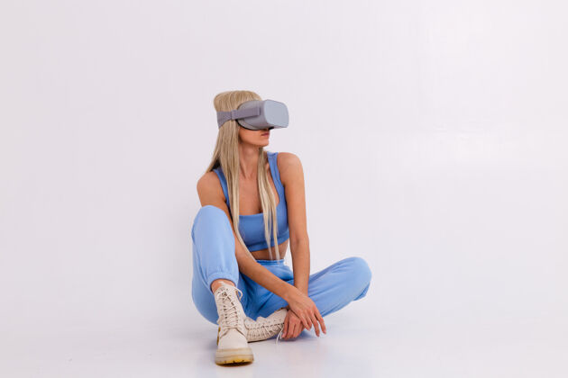 单身摄影棚照片中一个年轻迷人的女人穿着温暖的蓝色时尚西装戴着虚拟现实眼镜兴奋姿势Vr