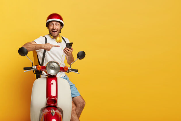 摩托车一个戴着红色头盔的摩托上快乐英俊的男司机的孤立镜头乘坐耳机运输
