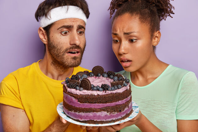 不健康一对活跃的情侣拿着一个大蛋糕摆姿势开胃菜休闲蛋糕