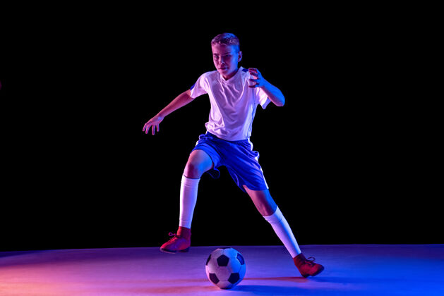 比赛在黑暗的工作室墙上 一个年轻的男孩像个足球运动员一样游戏身体跑步