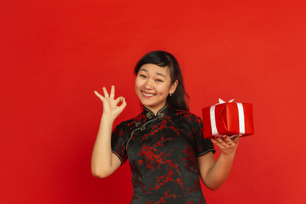 庆祝中国新年红色背景上孤立的亚洲少女肖像穿着传统服装的女模特带着礼品盒看起来很开心庆祝 节日 情绪表现得很好 微笑着欢呼年服装