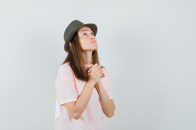 时尚身穿粉色t恤 戴着帽子 看上去充满希望的年轻女性双手合十祈祷正面图积极年轻休闲