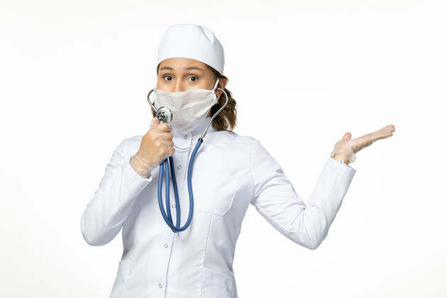 病毒正面图年轻女医生戴着防护性无菌口罩由于冠状病毒使用听诊器在白色办公桌上到期佩戴正面