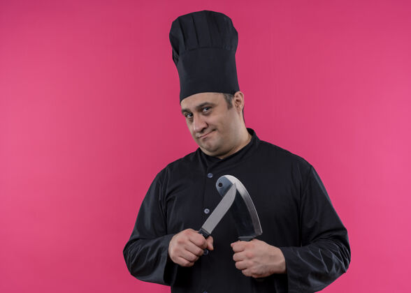 制服男厨师身穿黑色制服 头戴厨师帽 手持削尖刀 正脸站在粉色背景下看着镜头男脸厨师