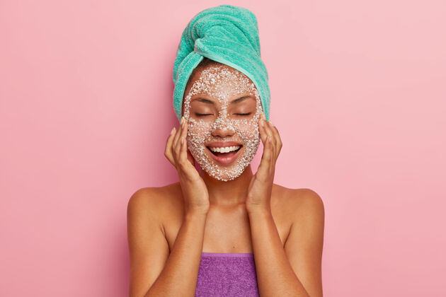站立积极的年轻女士用特殊的磨砂膏按摩脸部 减少脸颊上的黑点 感觉美容的乐趣 有皮肤问题 关心头发 用毛巾包着高分辨率剥皮女性面部