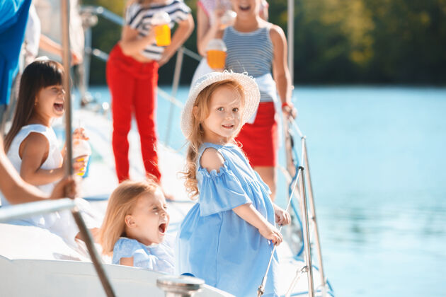 人孩子们在游艇上喝着橙汁青少年或少女们在蓝天下户外五颜六色的衣服孩子们的时尚 阳光明媚的夏天 河流和假日的概念欢乐朋友海洋
