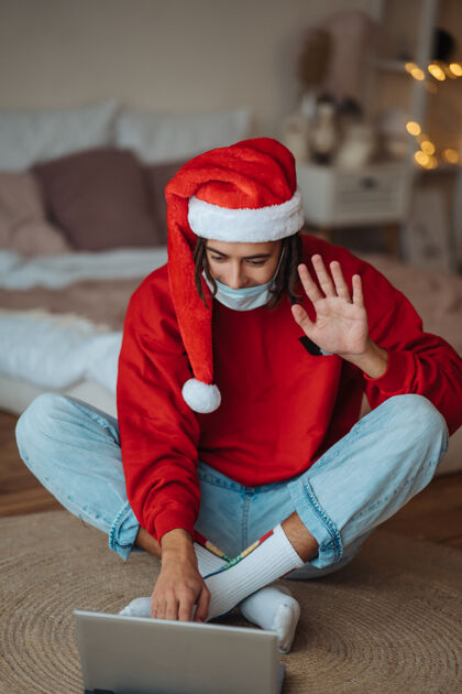 聋子在笔记本电脑旁戴着圣诞帽的家伙正在通过视频通话进行互动在家里过圣诞节是一种与世隔绝的生活在假期里是一种社交距离圣诞老人礼物笔记本电脑