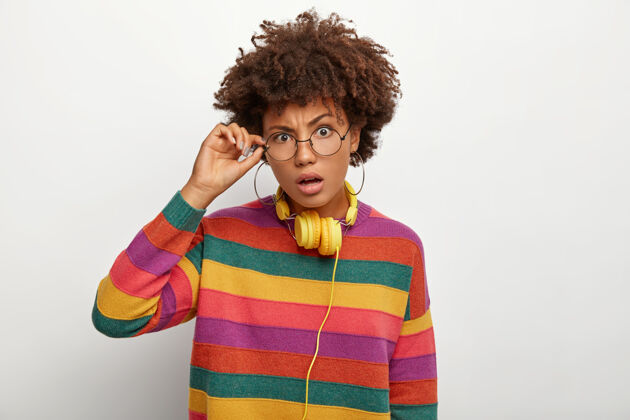 非洲人迷惑不解的卷发非裔美国妇女的横拍触到眼镜架 看得出奇 听得出奇 穿着条纹多色的套头衫女人理发美国人