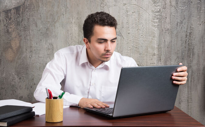男商人看着笔记本电脑 坐在办公桌旁高质量的照片办公室笔记本电脑书