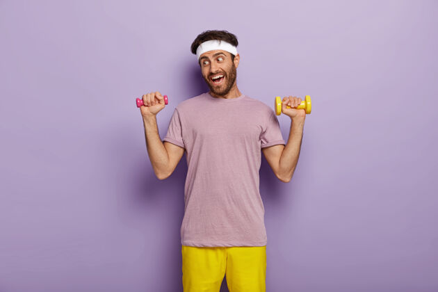 男性运动和娱乐的概念有趣的运动员练习哑铃 想要有强壮的手臂肌肉 穿休闲紫色t恤和黄色短裤紫色力量肌肉