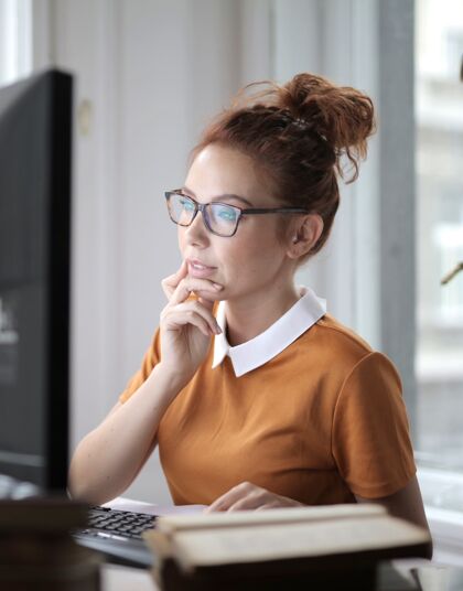 休闲一个体贴的年轻女性戴着眼镜在灯光下的电脑上工作的垂直镜头吸引力年轻网络