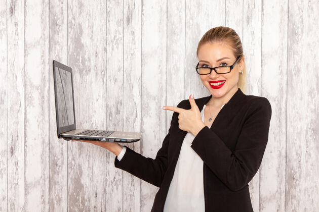 工作正面图穿着严苛衣服的年轻女商人黑色夹克在白墙上微笑着用她的笔记本电脑上班上班上班的女商人使用正面切肉刀