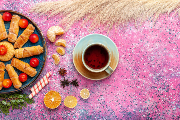 派顶视图甜甜可口的百吉饼在托盘内与酸李子和茶在淡粉色的桌子上李子水疗酸的