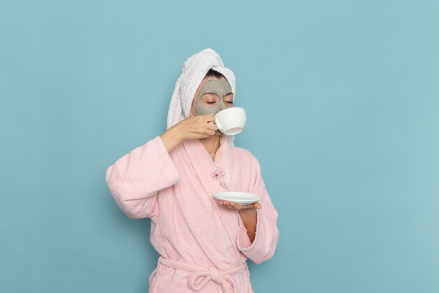 封面正面图身着粉色浴袍的年轻女性在蓝色墙壁上喝咖啡清洁美容自护霜淋浴脸饮用肖像