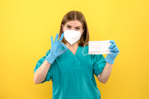 黄色黄色空间上戴着蓝色手套和面罩的女医生的前视图人专业微笑