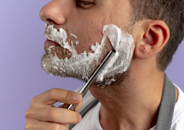男人理发师脸上涂着剃须泡沫 用剃刀在紫色的墙上刮胡子泡沫剃刀人