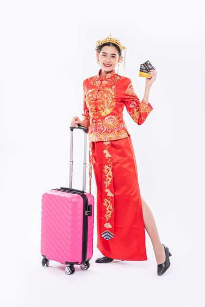微笑穿旗袍西服带皇冠的女士准备粉色旅行包和信用卡在中国的新年旅行文化手提箱节日