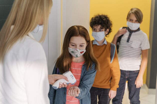 面罩带着医用面罩的女老师在学校检查学生的体温流行病教师新常态