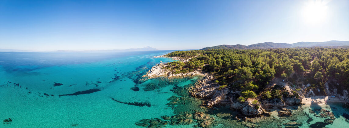 海岸爱琴海沿岸有蓝色透明的海水 周围绿树成荫 岩石 灌木丛和树木 从无人驾驶飞机上俯瞰希腊岩石山岩石