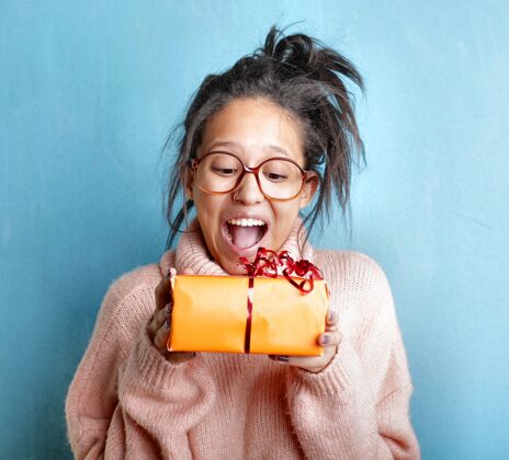 惊喜一位穿着粉色毛衣的年轻女性手持礼品盒表达着幸福年轻女士白色