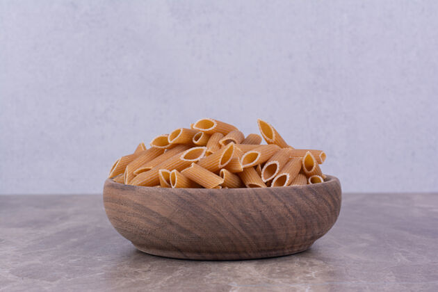 菜单在灰色表面上的一个朴素的木碗里放着潘恩意大利面健康质量生的
