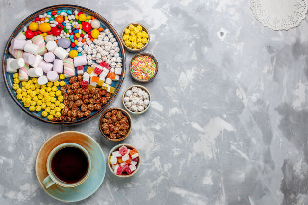 不同俯视图糖果组成不同颜色的糖果与棉花糖和一杯茶在白色的办公桌上糖果邦邦甜封棉花糖美味颜色