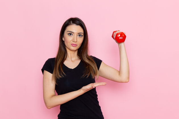 电器正面图年轻女性手持哑铃在浅粉色墙上运动员运动锻炼健康锻炼手持浅粉色女士