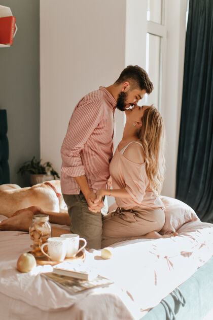 年轻在床上吃早餐这对夫妇在他们舒适明亮的卧室里 手牵着手 亲吻对方的眼睛成人床欢呼