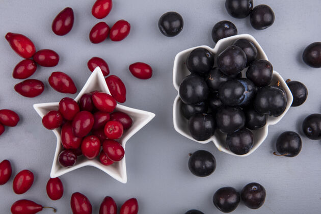 形状新鲜的红色山茱萸浆果在一个星形碗与黑葡萄在灰色的背景俯视图浆果观点新鲜