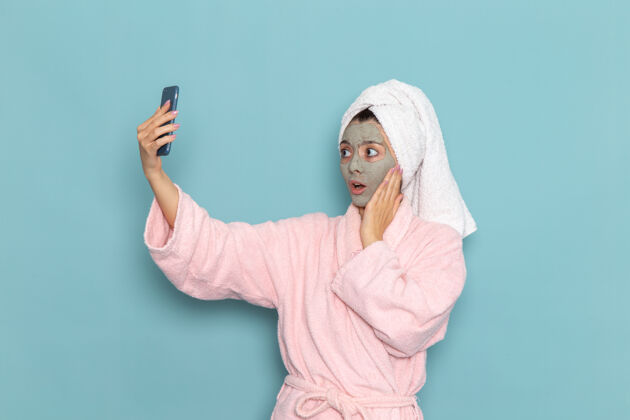 人正面图年轻女性穿着粉色浴袍淋浴后在浅蓝色墙上自拍美丽水自理淋浴干净视图脸女性