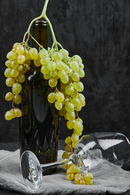 吃的白葡萄围绕着一瓶葡萄酒和一个空杯子在黑暗的表面水果葡萄酒新鲜的
